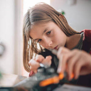 Girl wearing red hoodie building a robot at home as a school science project