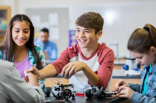 Confident Hispanic schoolboy and his classmates build robotic vehicles during technology class. They are assembling the robots.